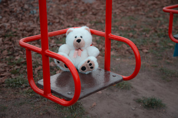 Close-up One teddy bear is sitting on a children's swing in red. The concept of sadness, loss,...