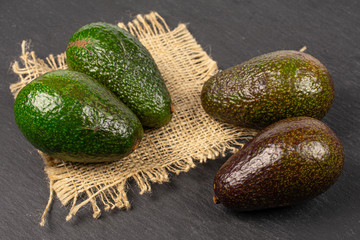 Group of four whole fresh green avocado on natural sackcloth on grey stone