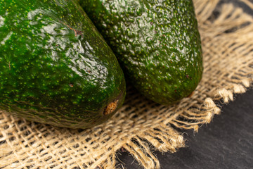 Group of two whole fresh green avocado on natural sackcloth on grey stone