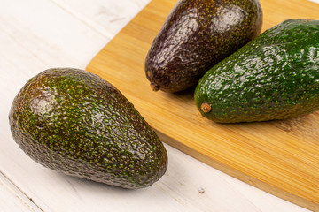 Group of three whole fresh green avocado on bamboo cutting board on white wood