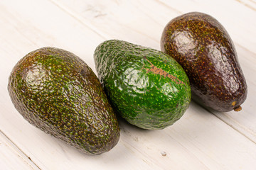 Group of three whole fresh green avocado on white wood