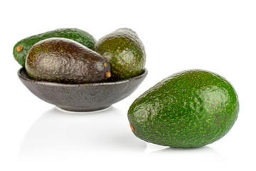 Group of four whole fresh green avocado in dark ceramic bowl isolated on white background