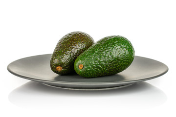 Group of two whole fresh green avocado on gray ceramic plate isolated on white background