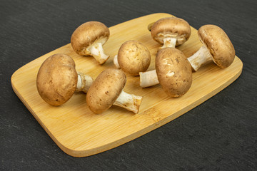 Group of seven whole fresh brown champignon on bamboo cutting board on grey stone