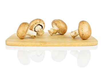 Group of four whole fresh brown champignon on bamboo cutting board isolated on white background