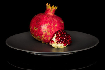 Group of one whole one piece of fresh red pomegranate on gray ceramic plate isolated on black glass