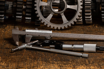 vernier callipers, micrometer and bore gauge on a workbench with gears in the background