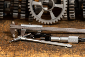 vernier callipers, micrometer and bore gauge on a workbench with gears in the background