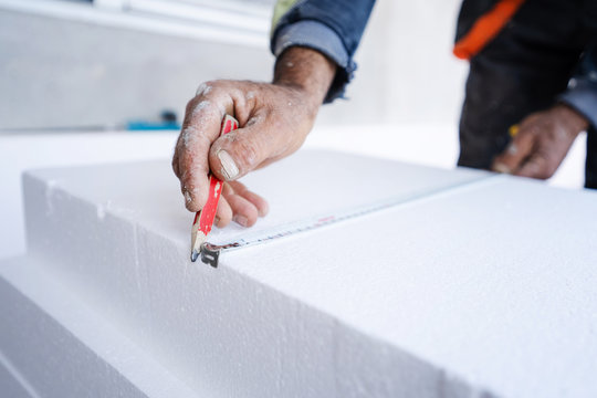 Worker use ruler measuring tape and pen to measure and mark the correct length of styrofoam during the wall insulation process at the construction site