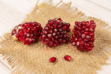 Group of five pieces of fresh red pomegranate on natural sackcloth on white wood