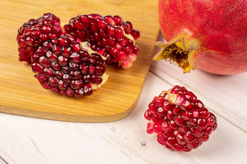 Group of one whole four pieces of fresh red pomegranate on bamboo cutting board on white wood