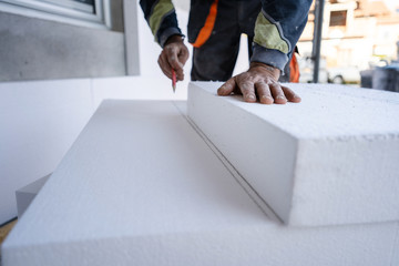 Worker use pen to mark the correct length and dimension of styrofoam during the wall insulation process at the construction site to cut the right size of the board - obrazy, fototapety, plakaty