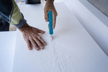 Construction worker using the hand saw to cut the styrofoam insulation panel table at the construction site in the insulating renovation procedure