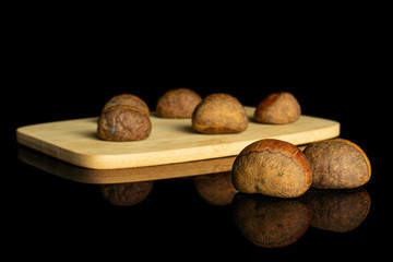 Group of seven whole sweet brown chestnut on bamboo cutting board isolated on black glass