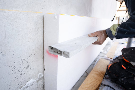 Construction Worker During The Styrofoam House External Wall Insulation. Contractor With Level Checking The Work In Progress Level Of The Boards