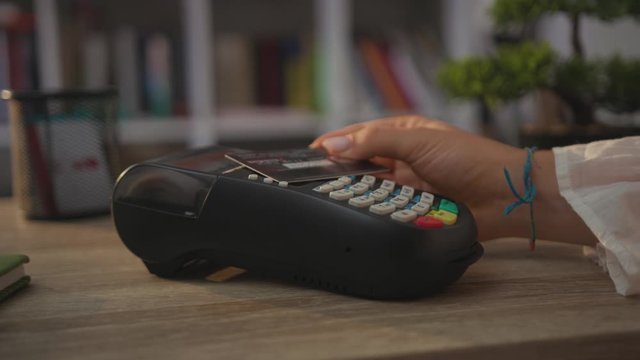 Young hands woman paying by credit card swiping with credit card on pos payment terminal on table customer machine money terminal cash client electronic slow motion