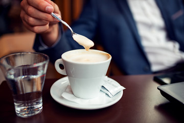 Businessman mixing sugar in coffee in modern cafe