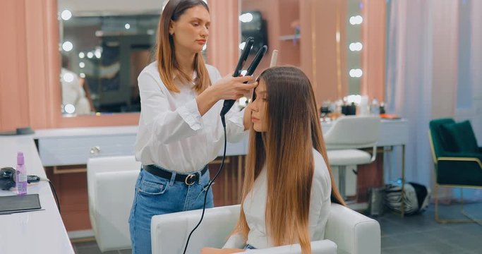 Hair straightening in a modern beauty salon. Professional hairdresser stylist combing strands of hair from the model.