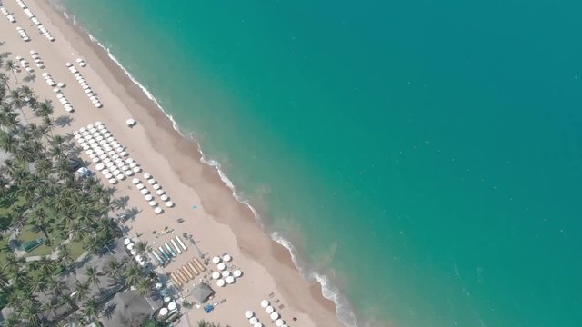 a flying camera shoots from top to bottom Nha Trang beach with many tourists, a wave and an umbrella
