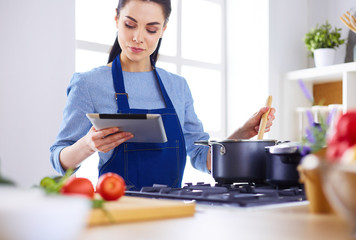 Young woman using a tablet computer to cook in her kitchen