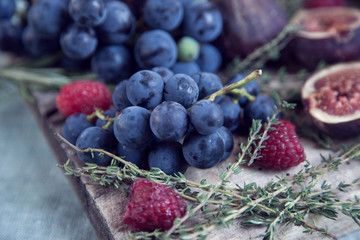 Shallow focus close up of a wood rustic chopping board of vibrant bunch of freshly picked organic dark blue purple table grapes with thyme raspberry and fig on display