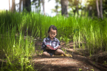 Cute little girl reading Bible and praying in nature with light in morning time. christian concept.