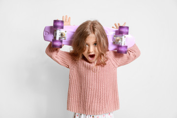 Surprised little girl with skateboard on light background © Pixel-Shot