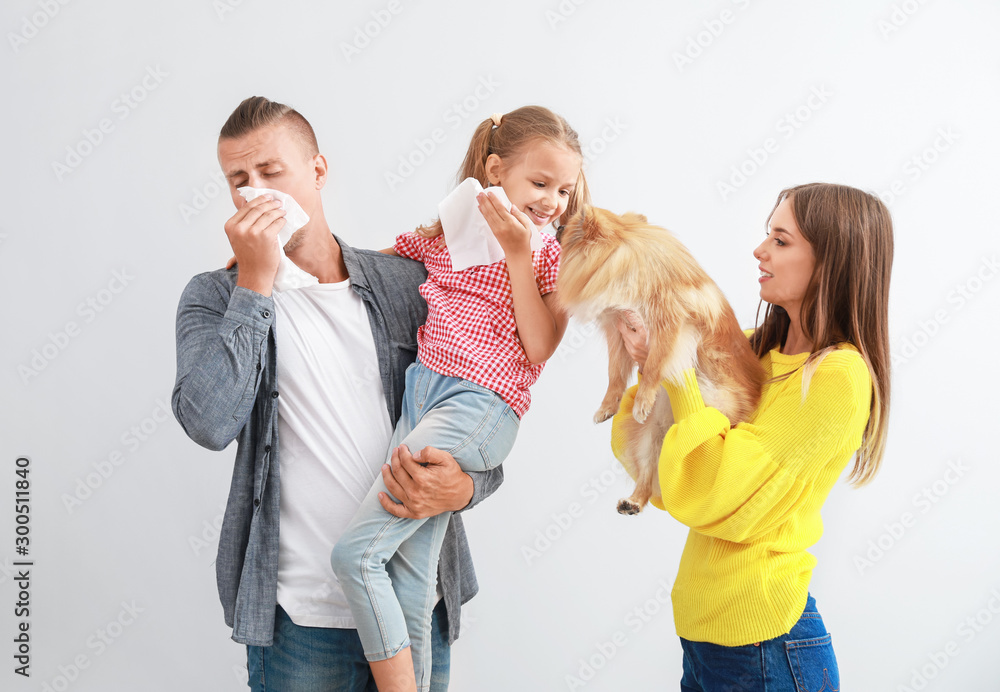 Wall mural Young woman with dog and husband with daughter suffering from pet allergy on light background