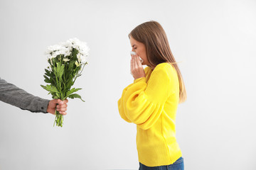 Man giving flowers to young woman suffering from allergy on light background