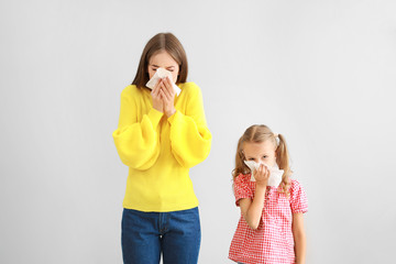 Young woman and girl suffering from allergy on light background