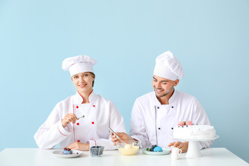 Young confectioners cooking tasty desserts against color background