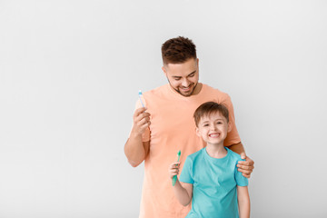 Portrait of man and his little son brushing teeth on light background