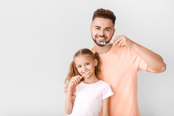 Portrait of man and his little daughter brushing teeth on light background