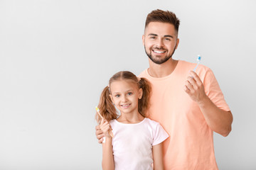 Portrait of man and his little daughter brushing teeth on light background