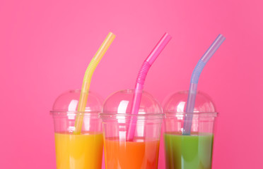 Plastic cups of fresh juices on color background