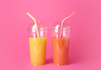 Plastic cups of fresh juices on color background