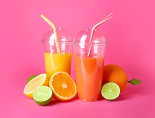Plastic cups of fresh juices with citrus fruits on color background