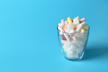 Glass with marshmallow and sugar on color background