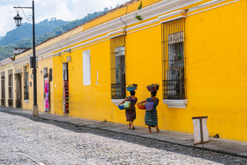 Dos mujeres mayas están caminando con sus cestas de frutas  en una calle en la ciudad de Antigua...