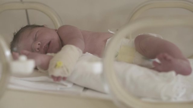 Hyperactive premature newborn baby sleeping during treatment in incubator at hospital intensive care unit, interior scene..