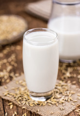 Old wooden table with fresh Oat Milk (close-up shot; selective focus)