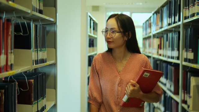 Woman reading a book in library. Portrait of college girl reading book in library. A young Asian female student searches for a book for her research project.