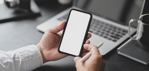 Cropped shot of professional businessman holding blank screen smartphone in dark modern office