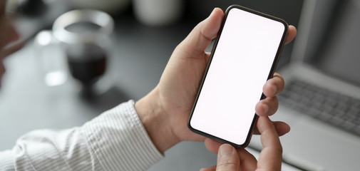 Cropped shot of professional businessman holding blank screen smartphone in dark modern office