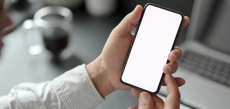 Cropped shot of professional businessman holding blank screen smartphone in dark modern office
