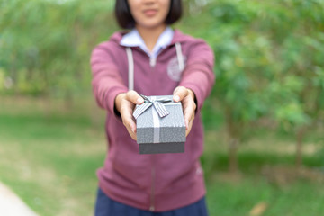 The girl's hand is giving a gift box for a special day or surprise or festival such as Christmas, New Year and Anniversary, making the recipient happy with the gift.