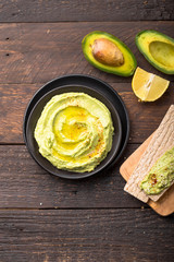 Two crackers with green  hummus, delicious cream of chickpeas and avocado on a wood background.