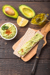 Two crackers with green  hummus, delicious cream of chickpeas and avocado on a wood background.