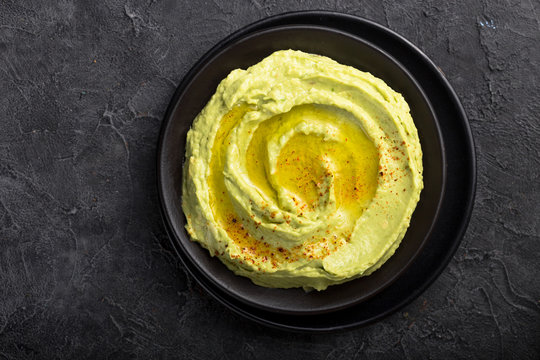 Bowl of green hummus, delicious cream of chickpeas and avocado on a stone  background.