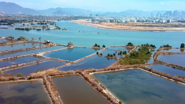 Abandoned shrimp farming ponds along polluted river on the outskirts of modern city aerial view. Fast growing south asian city concept.